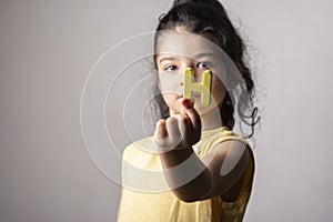 Cute little girl with H letter at hand wearing a yellow dress