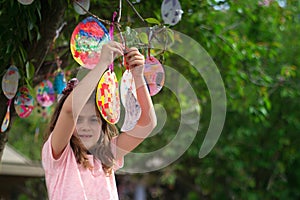 Cute little girl hanging on the tree her Easter cards in egg shape, for good luck and with good wishes