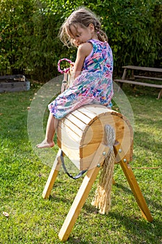 Cute little girl happily closing eyes when sitting on parents handmade wooden horse birthday present in garden.