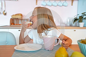 Cute little girl is having breakfast at home in the morning enjoying donut with tea. delicious food