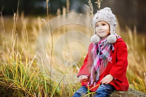 Cute little girl having fun on beautiful autumn day. Happy child playing in autumn park. Kid gathering yellow fall foliage.