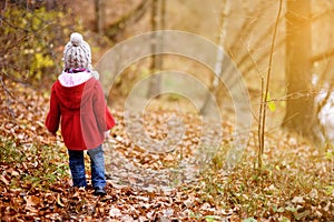 Cute little girl having fun on beautiful autumn day. Happy child playing in autumn park. Kid gathering yellow fall foliage.