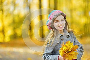 Cute little girl having fun on beautiful autumn day. Happy child playing in autumn park. Kid gathering yellow fall foliage.