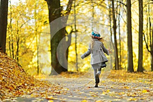 Cute little girl having fun on beautiful autumn day. Happy child playing in autumn park. Kid gathering yellow fall foliage.