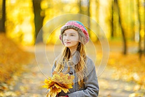 Cute little girl having fun on beautiful autumn day. Happy child playing in autumn park. Kid gathering yellow fall foliage.