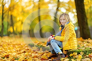 Cute little girl having fun on beautiful autumn day. Happy child playing in autumn park. Kid gathering yellow fall foliage.