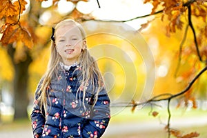 Cute little girl having fun on beautiful autumn day. Happy child playing in autumn park. Kid gathering yellow fall foliage.