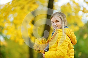 Cute little girl having fun on beautiful autumn day. Happy child playing in autumn park. Kid gathering yellow fall foliage.