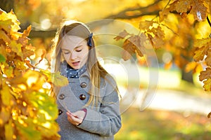 Cute little girl having fun on beautiful autumn day. Happy child playing in autumn park. Kid gathering yellow fall foliage.