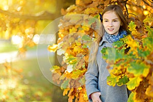 Cute little girl having fun on beautiful autumn day. Happy child playing in autumn park. Kid gathering yellow fall foliage.