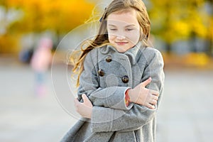 Cute little girl having fun on beautiful autumn day. Happy child playing in autumn park. Kid gathering yellow fall foliage.