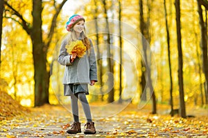 Cute little girl having fun on beautiful autumn day. Happy child playing in autumn park. Kid gathering yellow fall foliage.