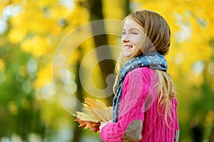 Cute little girl having fun on beautiful autumn day. Happy child playing in autumn park. Kid gathering yellow fall foliage.