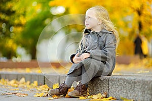 Cute little girl having fun on beautiful autumn day. Happy child playing in autumn park. Kid gathering yellow fall foliage.