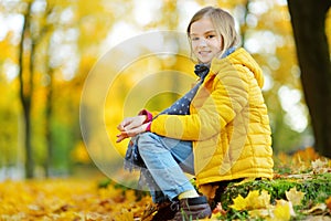 Cute little girl having fun on beautiful autumn day. Happy child playing in autumn park. Kid gathering yellow fall foliage.