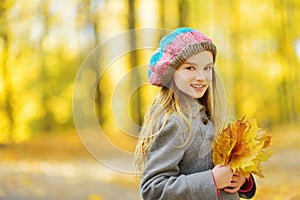 Cute little girl having fun on beautiful autumn day. Happy child playing in autumn park. Kid gathering yellow fall foliage.