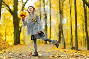 Cute little girl having fun on beautiful autumn day. Happy child playing in autumn park. Kid gathering yellow fall foliage.