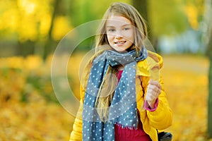 Cute little girl having fun on beautiful autumn day. Happy child playing in autumn park. Kid gathering yellow fall foliage.