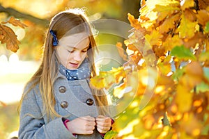 Cute little girl having fun on beautiful autumn day. Happy child playing in autumn park. Kid gathering yellow fall foliage.