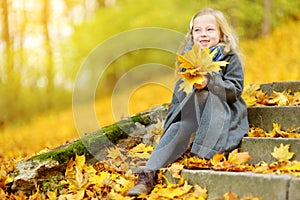 Cute little girl having fun on beautiful autumn day. Happy child playing in autumn park. Kid gathering yellow fall foliage.