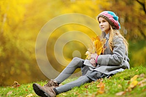 Cute little girl having fun on beautiful autumn day. Happy child playing in autumn park. Kid gathering yellow fall foliage.