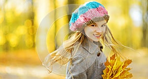 Cute little girl having fun on beautiful autumn day. Happy child playing in autumn park. Kid gathering yellow fall foliage.