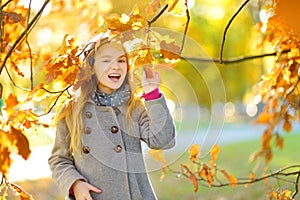 Cute little girl having fun on beautiful autumn day. Happy child playing in autumn park. Kid gathering yellow fall foliage.