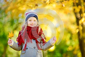 Cute little girl having fun on beautiful autumn day. Happy child playing in autumn park. Kid gathering yellow fall foliage.