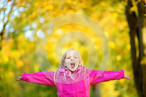 Cute little girl having fun on beautiful autumn day. Happy child playing in autumn park. Kid gathering yellow fall foliage.