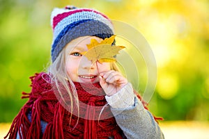 Cute little girl having fun on beautiful autumn day. Happy child playing in autumn park. Kid gathering yellow fall foliage.