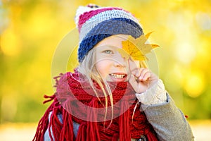 Cute little girl having fun on beautiful autumn day. Happy child playing in autumn park. Kid gathering yellow fall foliage.