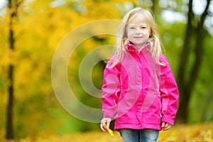 Cute little girl having fun on beautiful autumn day. Happy child playing in autumn park. Kid gathering yellow fall foliage.