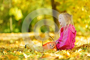 Cute little girl having fun on beautiful autumn day. Happy child playing in autumn park. Kid gathering yellow fall foliage.