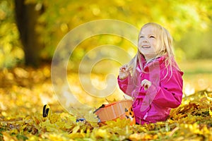 Cute little girl having fun on beautiful autumn day. Happy child playing in autumn park. Kid gathering yellow fall foliage.