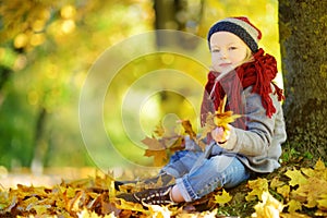 Cute little girl having fun on beautiful autumn day. Happy child playing in autumn park. Kid gathering yellow fall foliage.