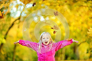 Cute little girl having fun on beautiful autumn day. Happy child playing in autumn park. Kid gathering yellow fall foliage.