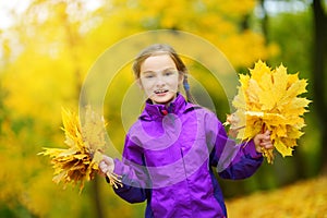 Cute little girl having fun on beautiful autumn day. Happy child playing in autumn park. Kid gathering yellow fall foliage.