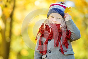 Cute little girl having fun on beautiful autumn day. Happy child playing in autumn park. Kid gathering yellow fall foliage.