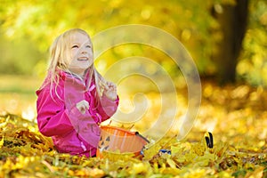 Cute little girl having fun on beautiful autumn day. Happy child playing in autumn park. Kid gathering yellow fall foliage.