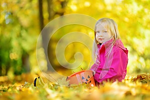 Cute little girl having fun on beautiful autumn day. Happy child playing in autumn park. Kid gathering yellow fall foliage.