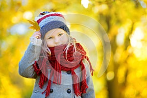 Cute little girl having fun on beautiful autumn day. Happy child playing in autumn park. Kid gathering yellow fall foliage.