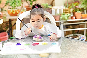 Cute little girl having fun, coloring with brush, playing and painting. Preschooler with paint at garden.