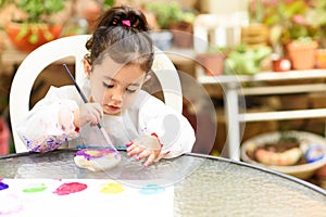 Cute little girl having fun, coloring with brush, playing and painting. Preschooler with paint at garden.