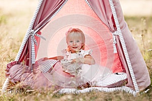 cute little girl is having fun near wigwam in a summer field on sunny day. Young family spending time together on