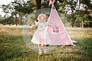 cute little girl is having fun near wigwam in a summer field on sunny day. Young family spending time together on