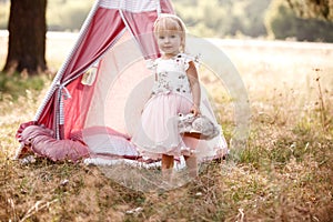 cute little girl is having fun near wigwam in a summer field on sunny day. Young family spending time together on