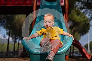 Cute little girl having fun on outdoor playground. Child on plastic slide.