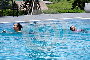 Cute little girl having fun swimming with her mother in the pool on a sunny day. Happy family, mother and her daughter playing in