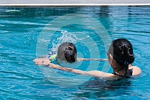 Cute little girl having fun swimming with her mother in the pool on a sunny day. Happy family, mother and her daughter playing in