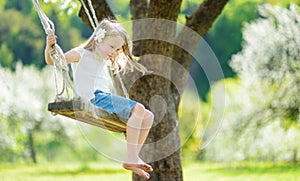 Cute little girl having fun on a swing in blossoming old apple tree garden outdoors on sunny spring day